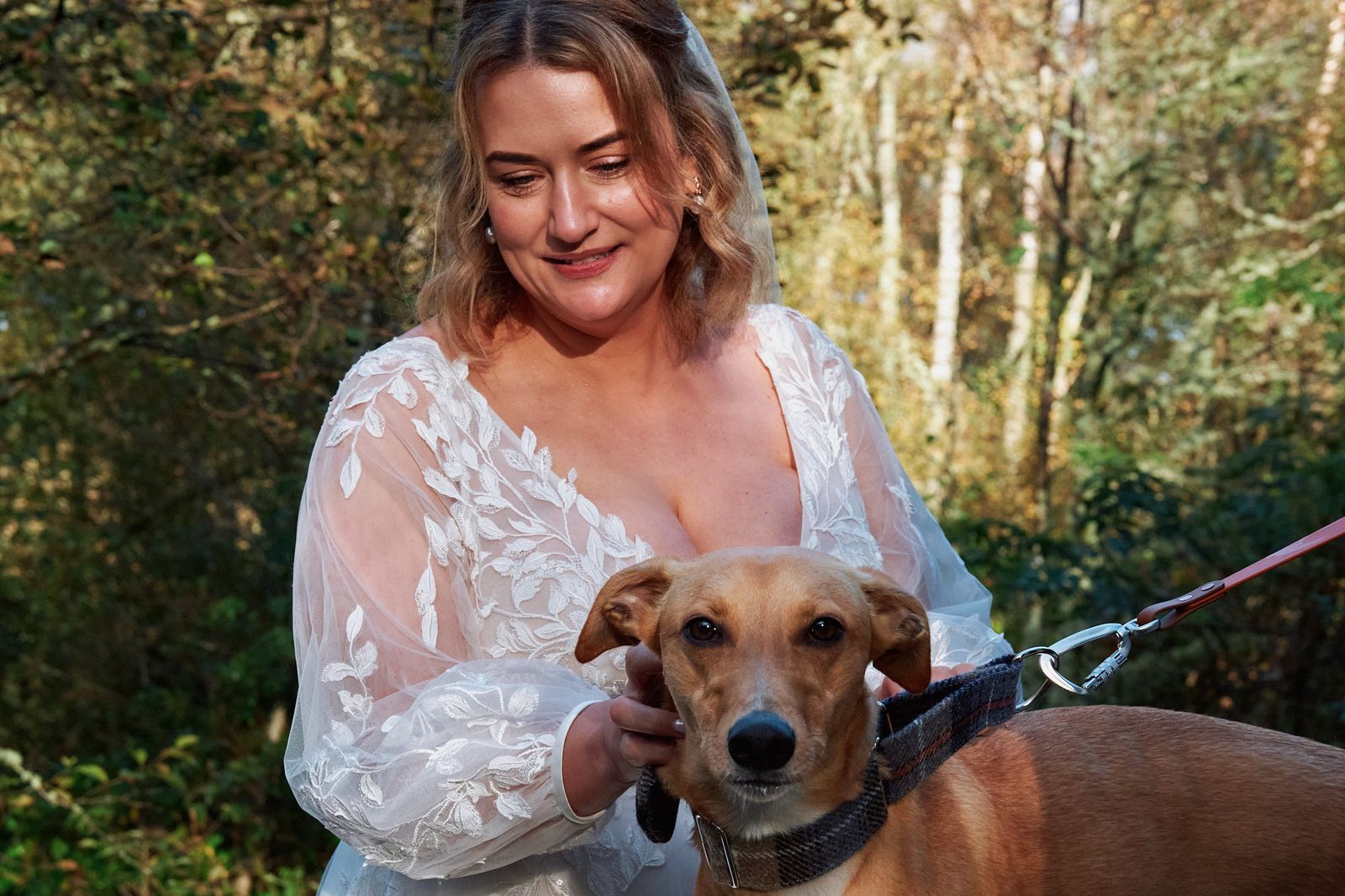 The bride smiling as she holds the lead of their dog