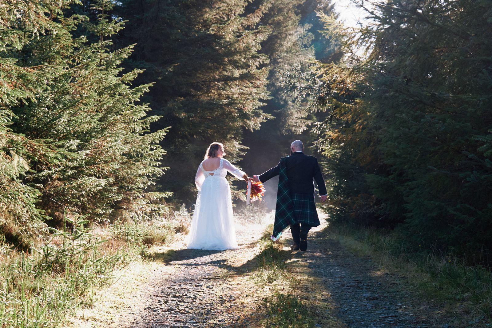 The couple walking hand in hand down a forest track