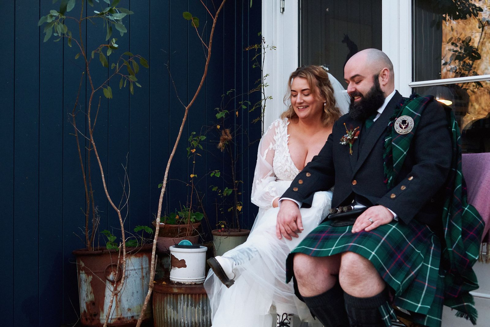 The couple sitting together outside a navy blue cottage