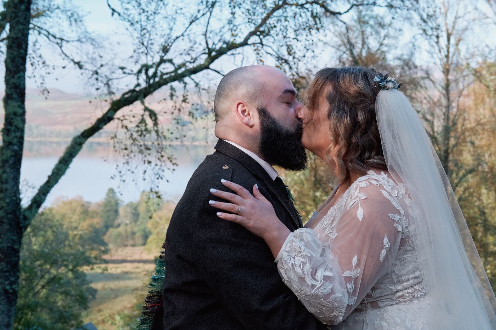 The couple embracing among the trees with the loch behind
