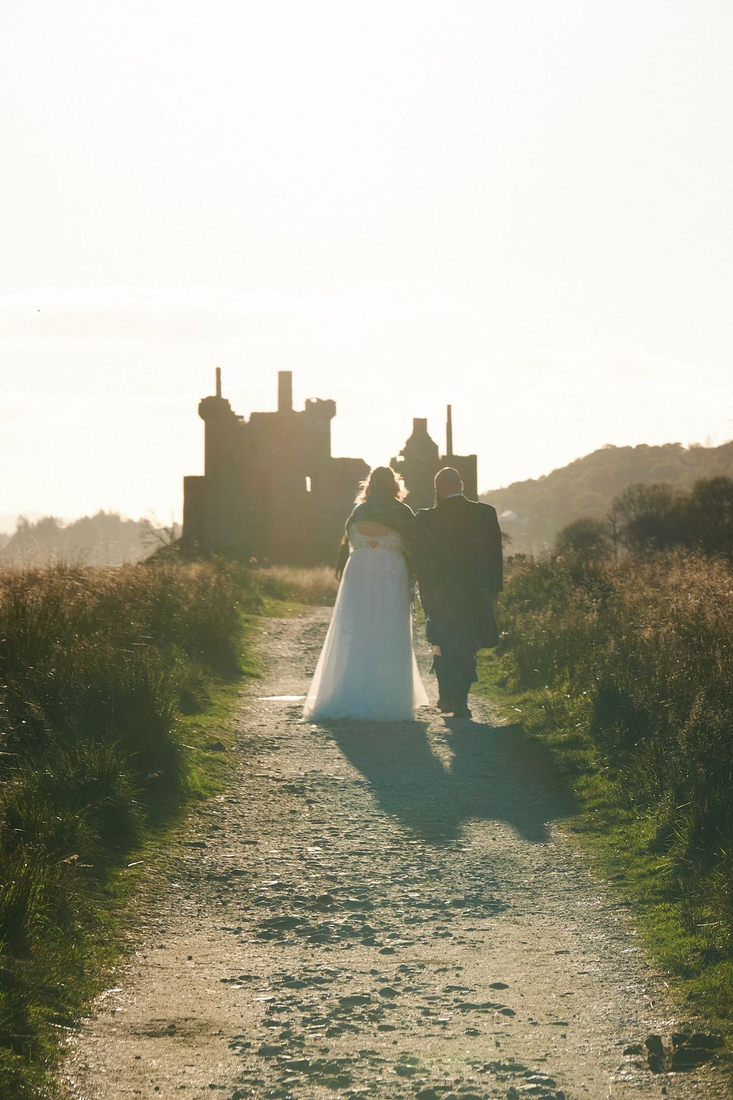 A couple walking down a path towards a castle silhouetted in evening light