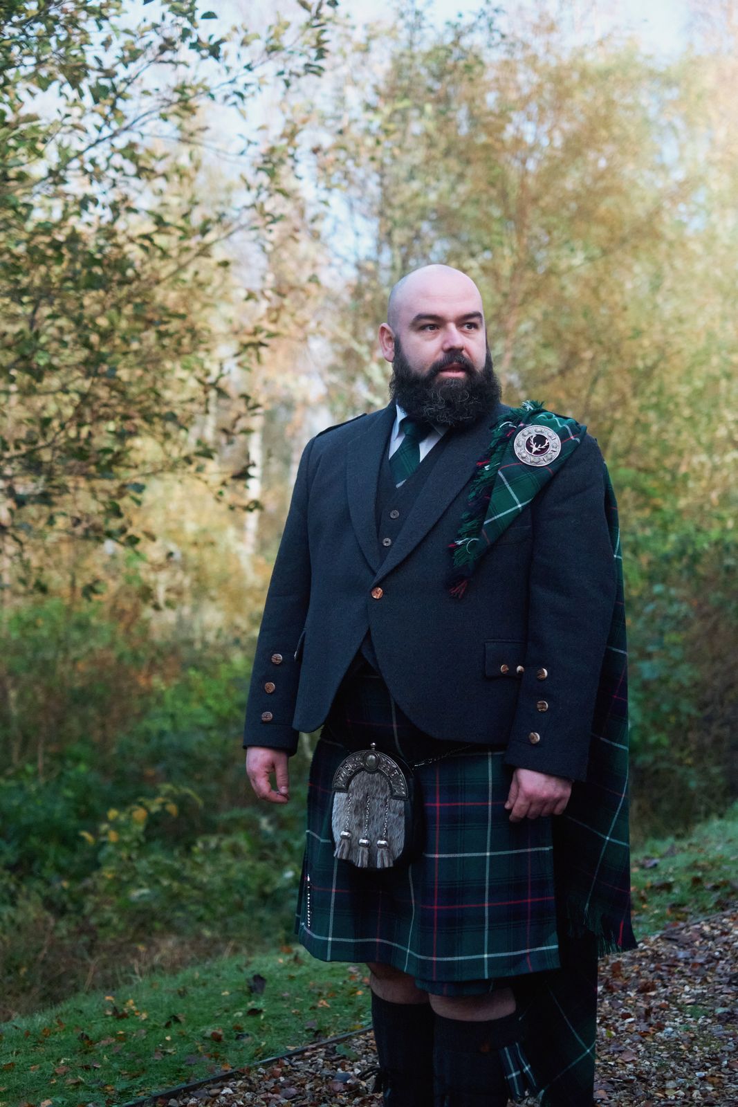 Groom in a kilt standing among autumn trees
