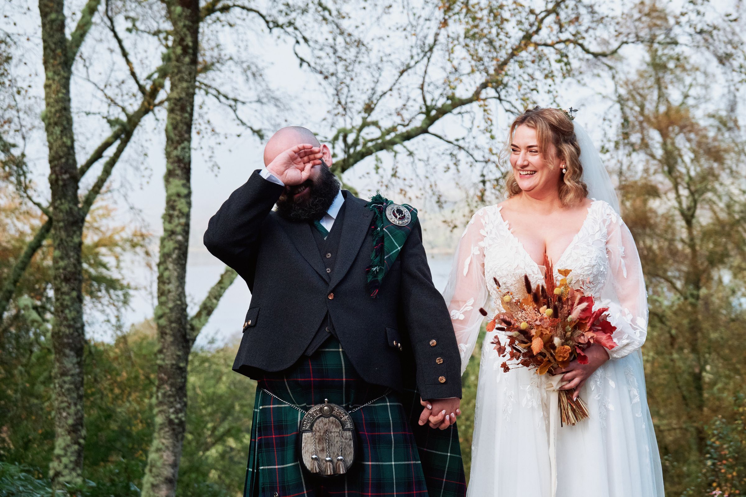 Groom in a kilt wiping away a tear beside his laughing bride